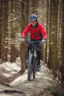 Vista frontal del ciclista de montaña que monta en el camino de tierra en el bosque - foto de stock
