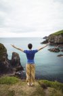 Rear view of man standing with arms outstretched on cliff — Stock Photo
