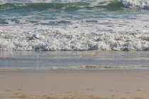 Ondas batendo na praia em um dia ensolarado — Fotografia de Stock