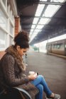 Жінка використовує телефон, сидячи на вокзалі — стокове фото