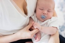 Close up of baby with dummy sleeping in mother 's arms at home — стоковое фото