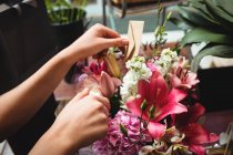 Manos de florista femenina arreglando ramo de flores en la florería - foto de stock