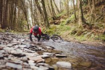 Mountain biker fallen in stream at forest — Stock Photo