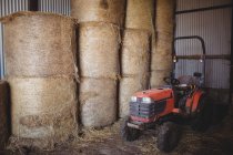 Montón de fardos de heno y tractor en granero - foto de stock