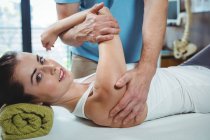 Fisioterapeuta masculino dando masaje de brazo a paciente femenina en clínica - foto de stock