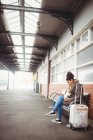 Женщина пользуется телефоном, сидя на платформе вокзала — стоковое фото