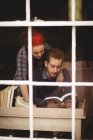 Young couple reading novel at home seen through window glass — Stock Photo