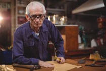 Senior-Schuhmacher schneidet in Werkstatt ein Stück Leder — Stockfoto