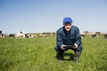 Retrato del trabajador agrícola usando tableta mientras se agacha en el campo herboso - foto de stock