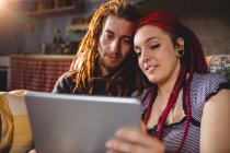 Jeune couple hipster utilisant une tablette numérique tout en étant assis à la maison — Photo de stock