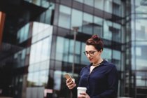Junge Frau fährt mit Handy gegen Bürogebäude — Stockfoto