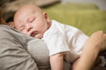 Cropped image of cute baby sleeping on mother in living room — Stock Photo