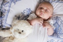 Baby sleeping on bed with teddy bear in bedroom at home — Stock Photo