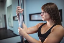Seitenansicht der Pole-Tänzerin, die im Fitnessstudio die Stange hält — Stockfoto