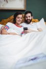 Пара с помощью мобильного телефона на кровати в спальне — стоковое фото