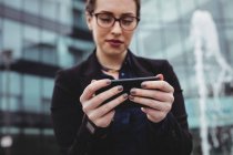 Businesswoman using mobile phone against office building — Stock Photo