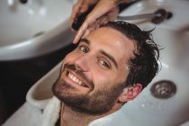 Retrato de homem sorridente recebendo sua lavagem de cabelo no salão — Fotografia de Stock