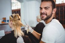 Портрет усміхненого чоловіка-перукаря фарбування волосся клієнта в салоні — стокове фото