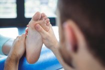 Мужской физиотерапевт делает женскому пациенту массаж ступней в клинике — стоковое фото