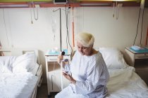 Старшая женщина смотрит на мобильный телефон в больнице — стоковое фото