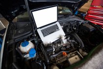 Auto con computer portatile sul cofano aperto per la manutenzione in garage di riparazione — Foto stock