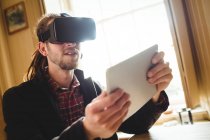 Молодой человек держит планшет, используя симулятор виртуальной реальности дома — стоковое фото
