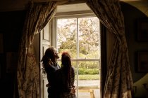 Casal jovem abraçando enquanto em pé pela janela em casa — Fotografia de Stock