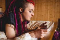Jeune femme utilisant une tablette numérique sur le lit à la maison — Photo de stock
