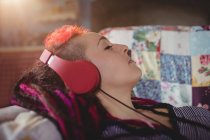 Junge Frau hört Musik während sie es sich zu Hause auf dem Sofa gemütlich macht — Stockfoto