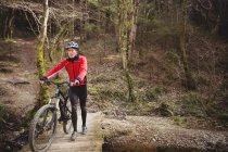 Mountain biker walking with bicycle on footbridge in forest — Stock Photo