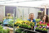 Two female florists smiling while checking plants in garden centre — Stock Photo