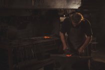 Schmied arbeitet in Werkstatt an einer erhitzten Eisenstange — Stockfoto
