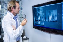 Вдумчивый дантист осматривает рентген на мониторе в клинике — стоковое фото