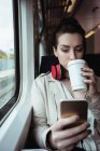 Giovane donna che utilizza il telefono cellulare mentre beve caffè in treno — Foto stock