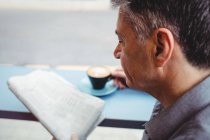 Primer plano del hombre leyendo el periódico y sosteniendo la taza de café en la cafetería - foto de stock