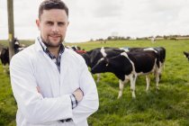 Ritratto di giovane veterinario in piedi contro mucche sul campo — Foto stock