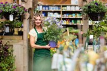 Portrait of female florist holding potted plant in garden centre — Stock Photo