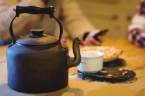 Teapot and cup on a table at home with people in background — Stock Photo