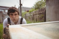 Carpenter blowing sawdust on wooden door — Stock Photo
