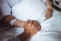 Старший мужчина держит за руки пожилую женщину в больнице — стоковое фото