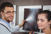 Retrato del fisioterapeuta explicando la radiografía de columna vertebral a una paciente femenina en la clínica - foto de stock
