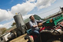 Incline a imagem do fazendeiro montando quadbike no campo contra o céu — Fotografia de Stock