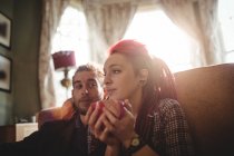 Frau hält Kaffeetasse, während der Mann sie zu Hause auf dem Sofa ansieht — Stockfoto