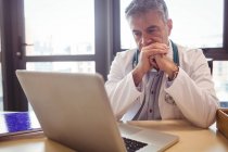 Doctor usando laptop en su escritorio en el hospital - foto de stock