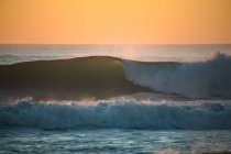 Ondas batendo ao pôr do sol na praia — Fotografia de Stock