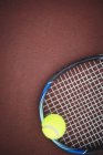Tennis ball and racket on brown ground in sport court — Stock Photo