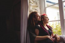 Joven pareja hipster sentada junto a la ventana en casa - foto de stock