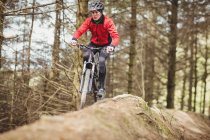 Front view of mountain biker riding by trees in forest — Stock Photo