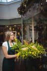 Floristería femenina arreglando flores en jarrón en su tienda de flores - foto de stock