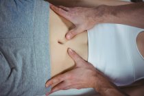 Обрезанное изображение мужского физиотерапевта, делающего массаж желудка пациентке — стоковое фото